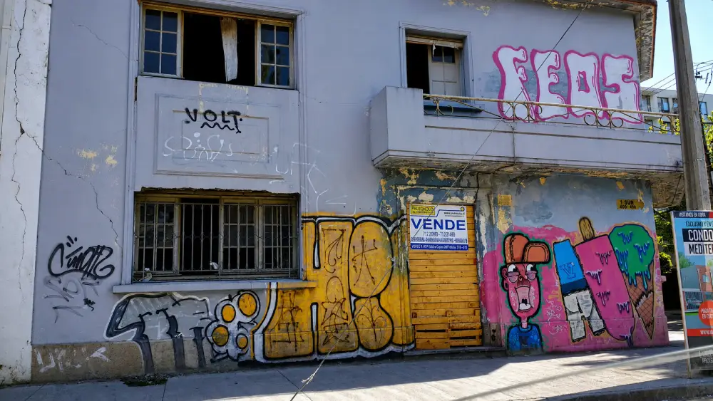 Fotografía documental de una fachada abandonada con grafitis coloridos y letrero de venta en la calle 1 Sur de Talca, registro del patrimonio dañado post-terremoto.